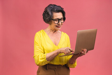 Senior aged business woman with laptop. Grandmother isolated over pink background.