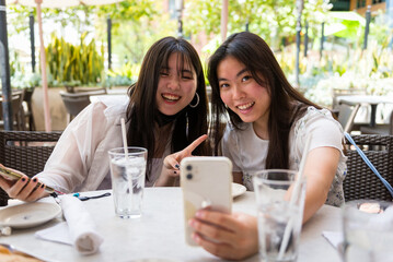 Two young asian girls taking selfie at a outdoor restaurant table