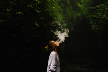 Naklejka premium Young woman smokes a vape in the jungle on a tropical island, Bali.