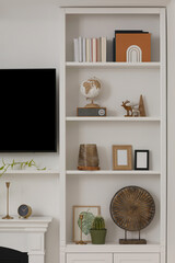 Stylish shelves with different decor elements and TV set in room. Interior design