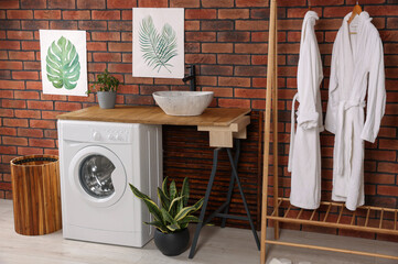 Washing machine and wooden rack with terry bathrobes indoors. Laundry room interior design