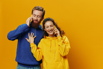 Fototapeta premium Woman and man cheerful couple with phones in hand talking on cell phone crooked smile cheerful, on yellow background. The concept of real family relationships, talking on the phone, work online.