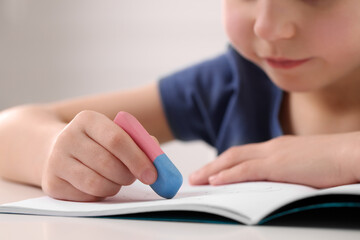 Fototapeta premium Little boy erasing mistake in his notebook at white desk, closeup