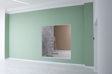 Green wall with opening for fake window and ladder in room during repair