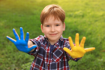 Little boy with hands painted in Ukrainian flag colors outdoors. Love Ukraine concept