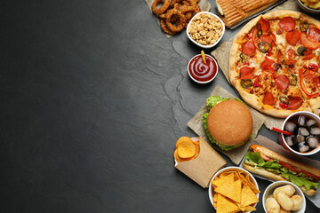 Pizza, burger and other fast food on black table, flat lay with space for text