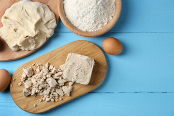 Compressed yeast, eggs, dough and flour on light blue wooden table, flat lay. Space for text