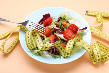 Healthy salad with measuring tape on orange background. Diet concept