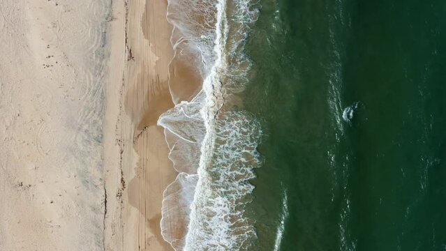 Dolly in bird's eye aerial shot of the tropical Rio Grande do Norte, Brazil coastline with golden sand, turquoise clear water and waves crashing on shore in between Baia Formosa and Barra de Cunha&uacute;