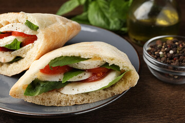 Delicious pita sandwiches with mozzarella, tomatoes and basil on wooden table, closeup