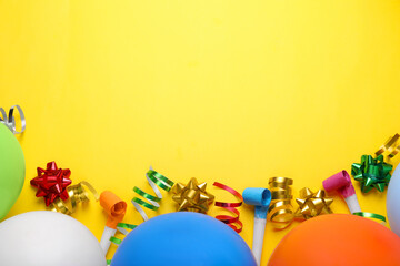 Balloons, party blowers and streamers for birthday party on yellow background, flat lay. Space for text