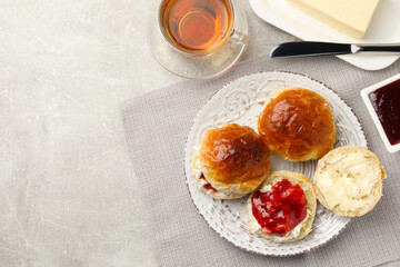 Freshly baked soda water scones with cranberry jam, butter and cup of tea on light grey table, flat lay. Space for text