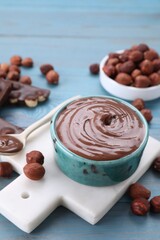 Bowl with tasty paste, chocolate pieces and nuts on light blue wooden table