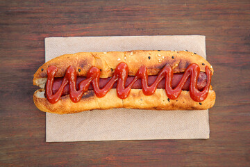 Fresh tasty hot dog with ketchup on wooden table, top view