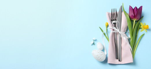 Set of cutlery, Easter eggs and flowers on light blue table, top view. Banner design with space for text