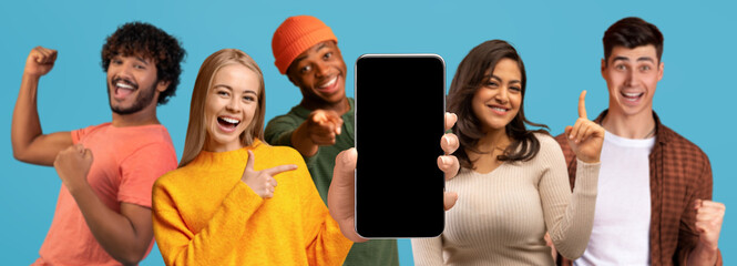 Obraz premium Glad excited millennial multiethnic people show smartphone with blank screen make victory and success gesture