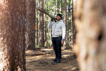 Hombre sonriente cargando troncos de madera en el bosque viendo a cámara cuerpo completo