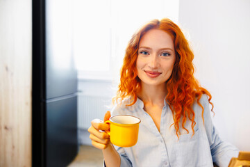 Beautiful young woman drinks coffee sitting by the window. Beautiful teenager sitting by the window having a hot drink.