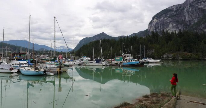Squamish Harbour view with boats and mountains in background. Woman using phone taking photos of scenic landscape, British Columbia, Canada