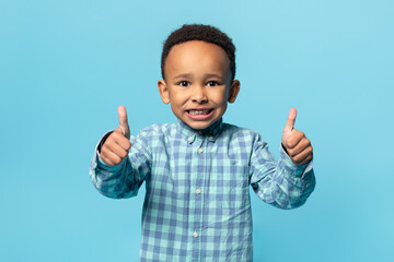 I like it. Happy african american adorable boy showing thumbs up and widely smiling, posing over...