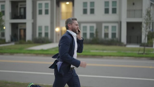 Man in suit in a hurry, calling phone and running. Running business man with phone outdoor. Running businessman talking on phone. Middle aged business man hurry late and talking on phone. Slow motion.