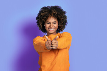 Positive african american woman showing thumb ups on purple