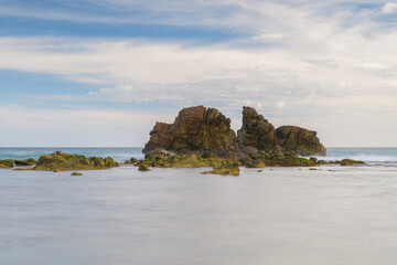 A beach with moss covered rocks and a sunset in the background