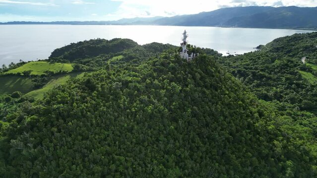 Cinematic Birdseye Aerial View of white Bote Lighthouse atop jungle-covered mountains with pristine island background of the calm ocean bay and rainforest. Bato, Catanduanes.