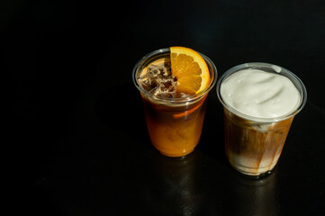 A plastic cup of orange coffee with an orange slice on the side