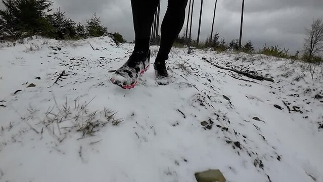 Close up front view slow motion of a trail runner on steep wintery forest downhill trail. Shoes are red and the runner applies a forefoot or midfoot strike.