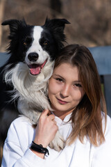 Caucasian woman hugging her dog Border Collie while sitting on a bench in autumn park.