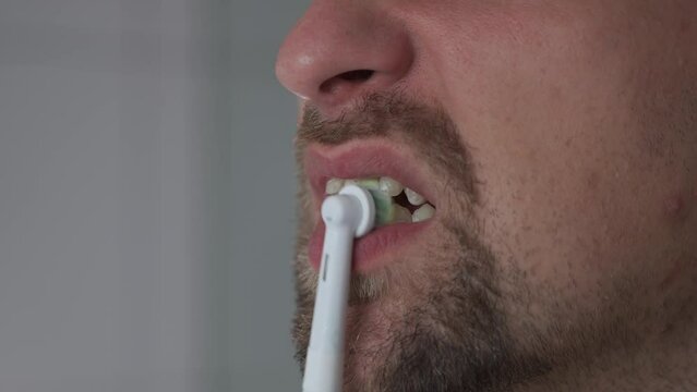 Theme of brushing and whitening teeth with a modern electric toothbrush. Close-up of a man cleaning his teeth with an ultrasonic dental brush. Morning routine, oral hygiene. Oscillating toothbrush. 