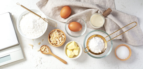 Baking and cooking ingredients, butter flour eggs and slivered almond with digital scale and utensil on marble table