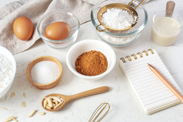 Baking pastry or cake ingredients, flour, brown sugar, milk on marble table with notebook and pen