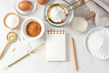 Baking pastry or cake ingredients with notebook and pen, sifting flour, brown sugar, eggs and milk with utensil on marble table