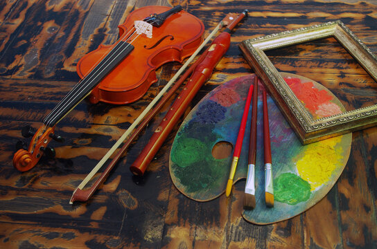Music and painting, Art attributes. Violin, bow, pipe, art palette, brushes, picture frame on a wooden table.