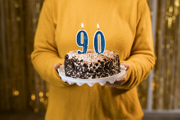 Happy ninetieth birthday. Woman holding fresh delicious birthday cake with burning candle number...