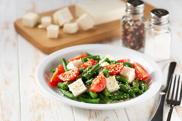 Fresh vegetarian vegetable salad with with tomatoes, feta and sesame seeds on a white wooden table, healthy food.