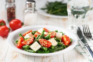 Fresh vegetarian vegetable salad with with tomatoes, feta and sesame seeds on a white wooden table, healthy food.