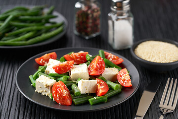 bowl of salad with with tomatoes, feta and sesame seeds on a black wooden table.