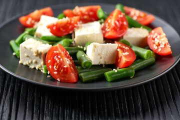 Green beans salad with feta on a black plate. Plate with delicious green beans salad on wooden table, closeup.