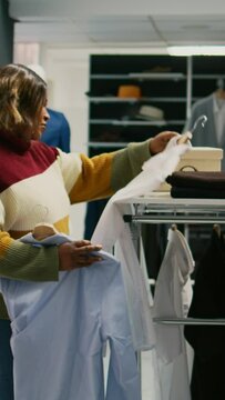 Vertical video: Modern client looking at shirts hanging in clothing store, young woman shopping for formal clothes to increase wardrobe. Shopping center customer buying modern fashion collection.