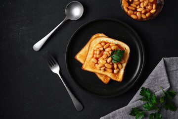Toast bread with baked beans with parsley on plate on black table. top view, copy space