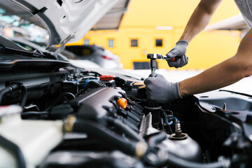 Professional car mechanic using a wrench for working on the engine of the car in the garage for car...