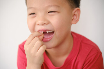 Cute Asian happy smiling schoolboy child showing missing teeth, Little kid losing his baby teeth and holding missing tooth, Dental care for children concept, Selective focus