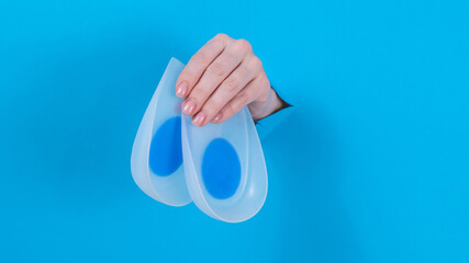 Woman holding orthopedic silicone heel pads. A woman's hand sticks out of a hole in a cardboard...