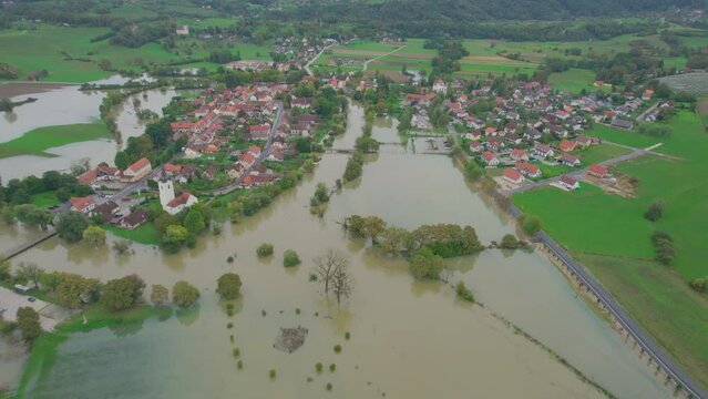 AERIAL: Picturesque village surrounded by floodwaters of overflowing rivers. Raised river levels spilled over their banks and inundated green meadows at riverside after abundant rainfall in autumn.