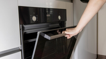 A woman's hand opens the door of a modern electric oven in the kitchen.