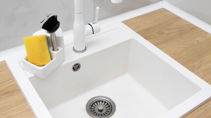 Beautiful kitchen interior of a white sink with a water faucet, sponge and brush for washing dishes...