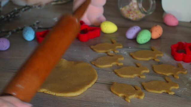 Womens hands close-up kneading ginger dough and carving figurines from it. The shapes of rabbit. Cutting sugar cookie dough with Easter shaped cookie cutters. Preparation for Easter. Holidays baking.